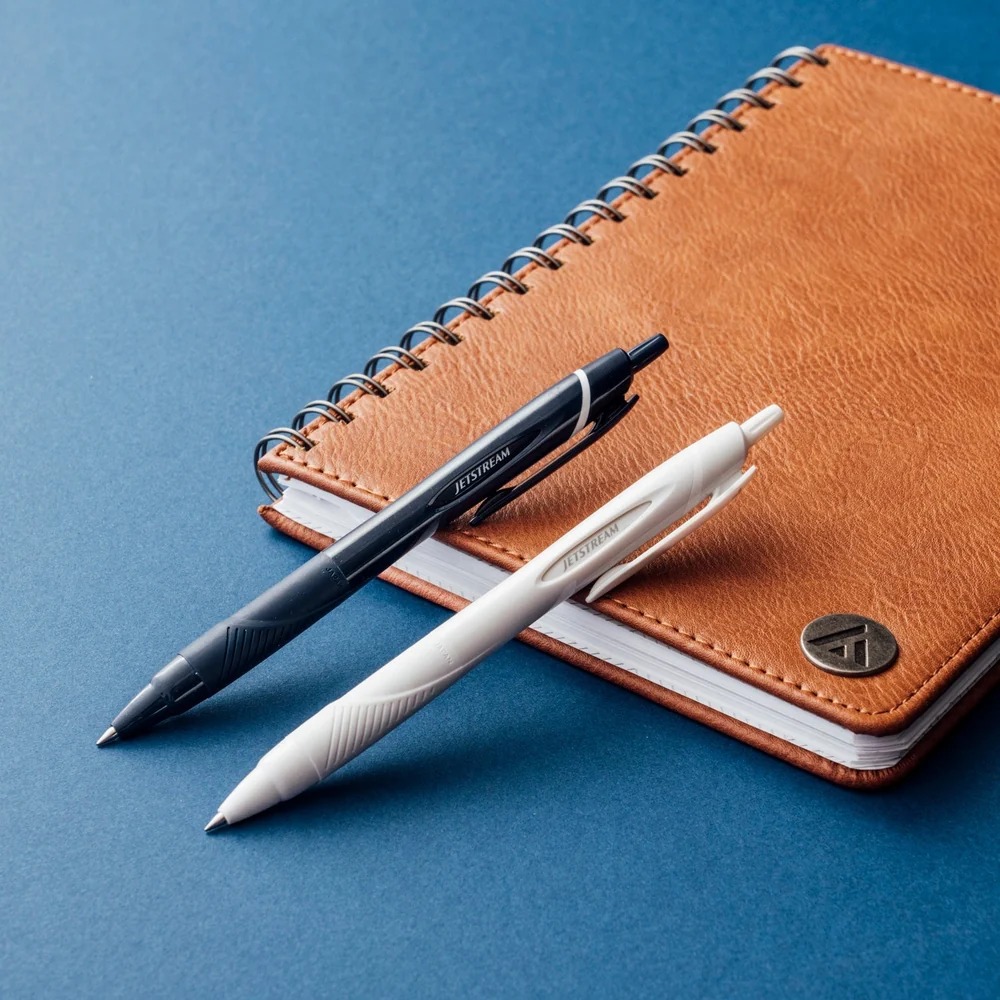 Navy and white pens resting on a brown notebook.